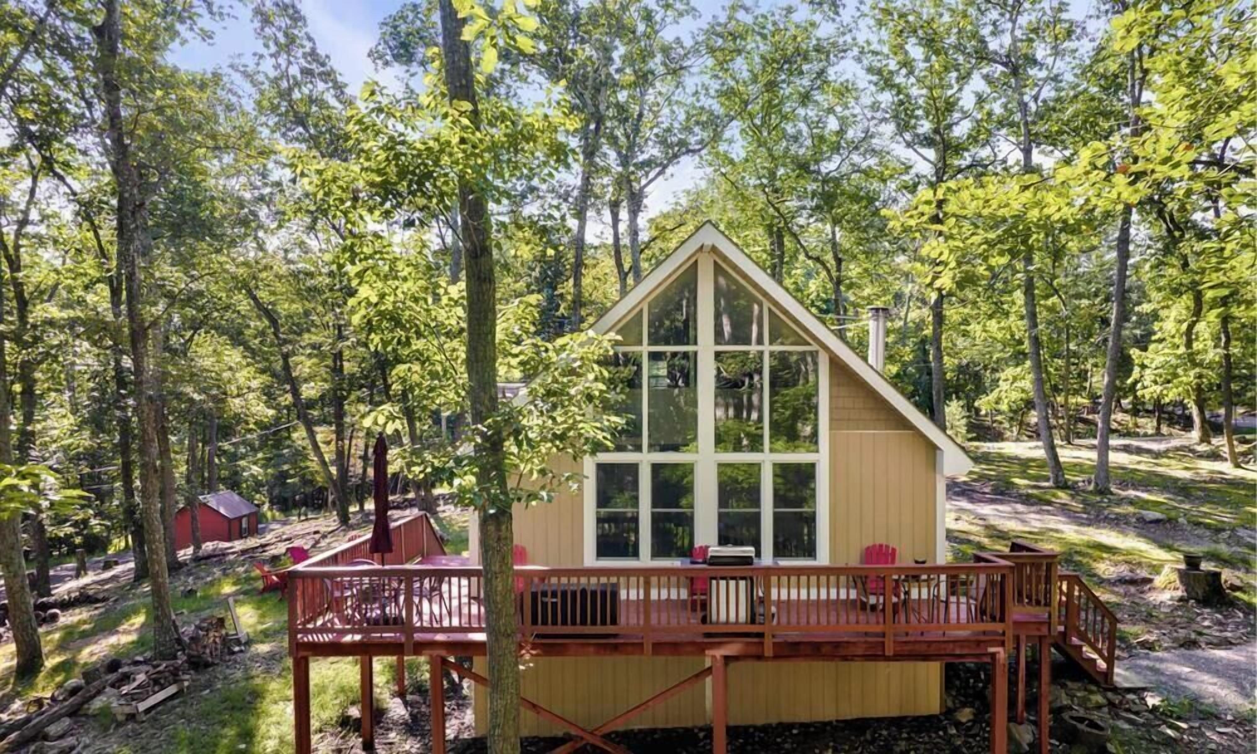 A cabin with a wooden deck, surrounded by trees.