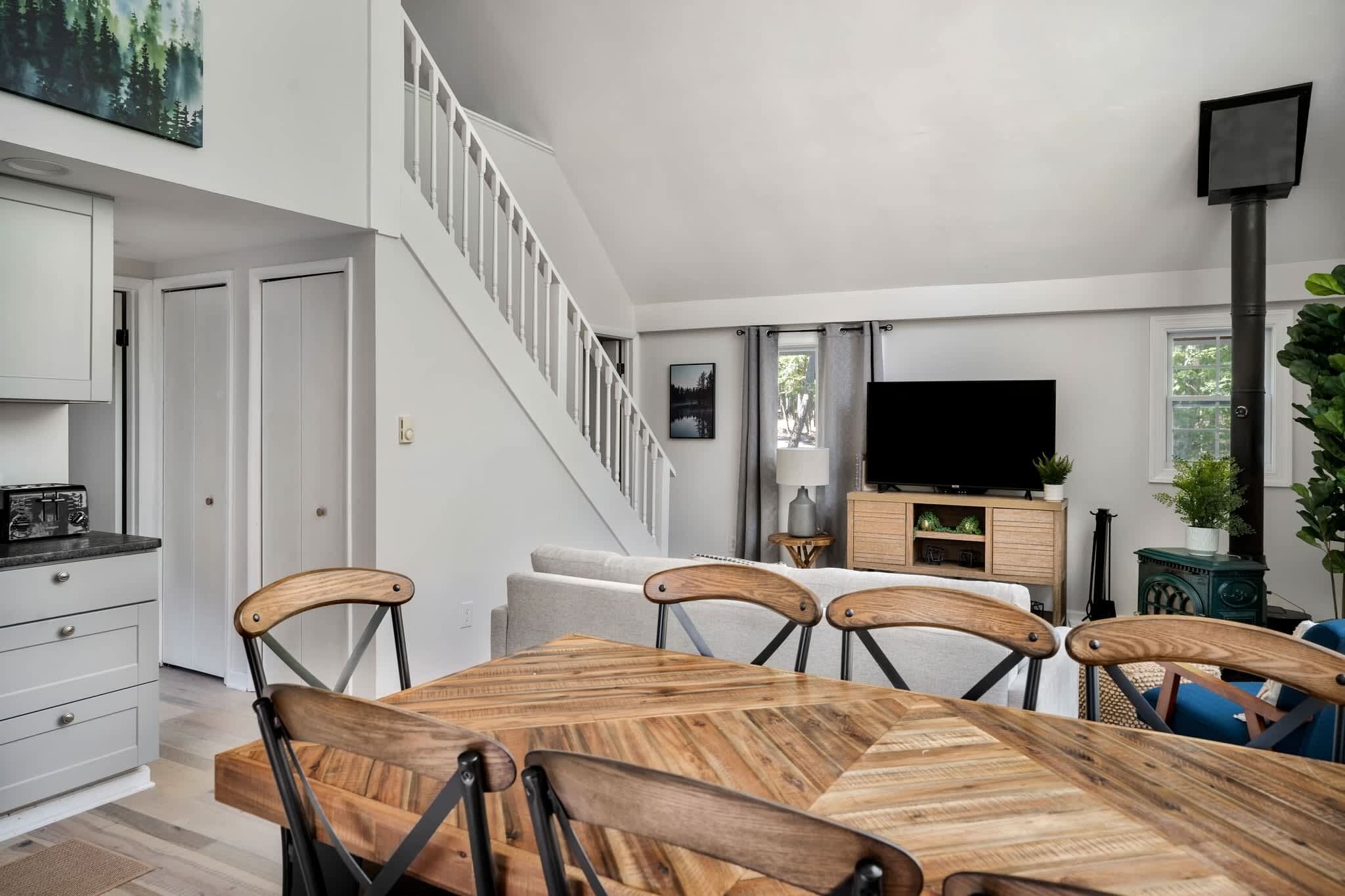 A modern living room with a wooden dining table, a TV, and a staircase leading to another level.