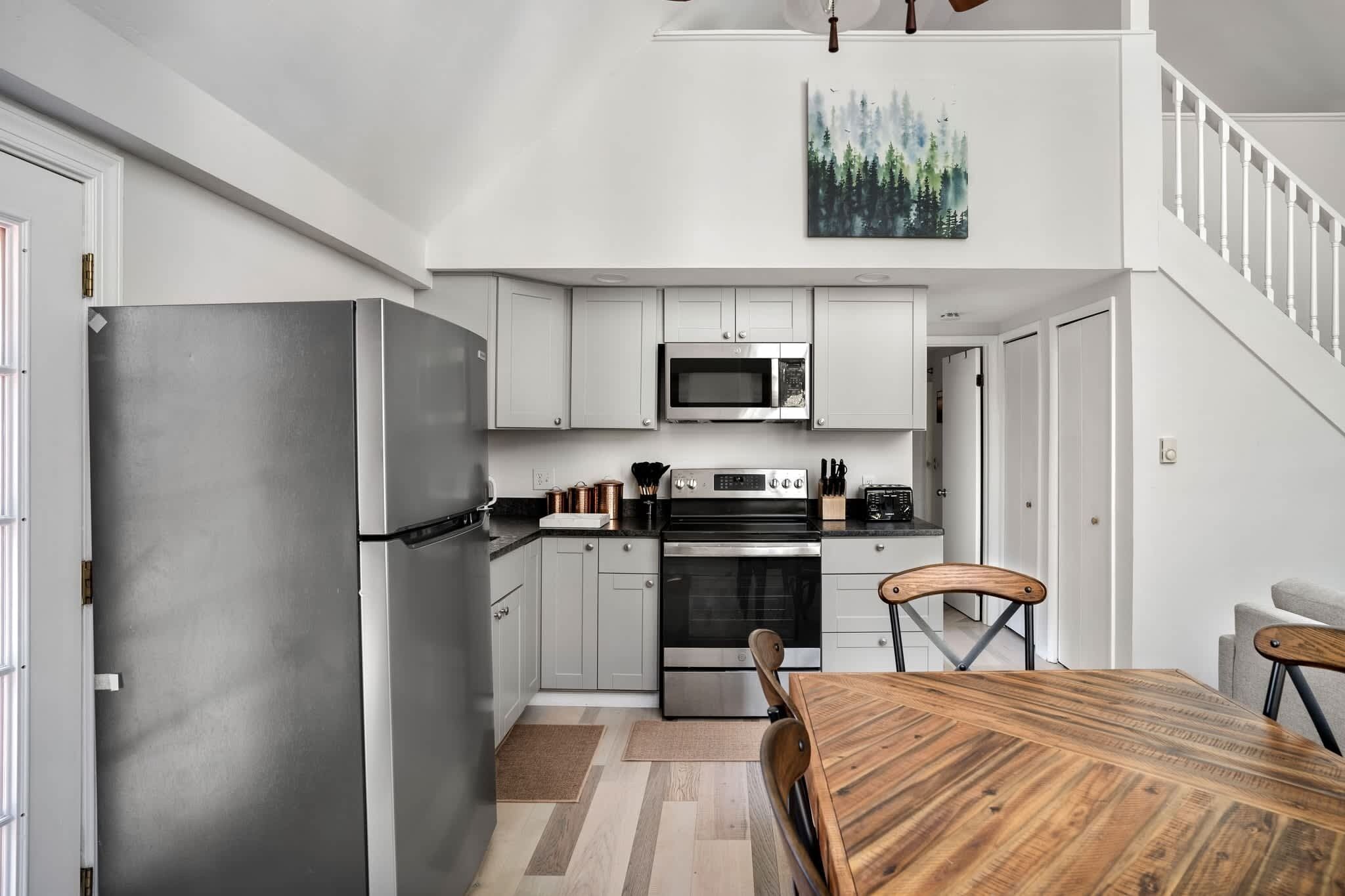 Una cocina moderna con armarios blancos, electrodomésticos de acero inoxidable y una mesa de comedor de madera.