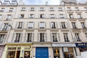 Un immeuble à plusieurs étages dont le rez-de-chaussée abrite des commerces, notamment une pharmacie et une boutique.