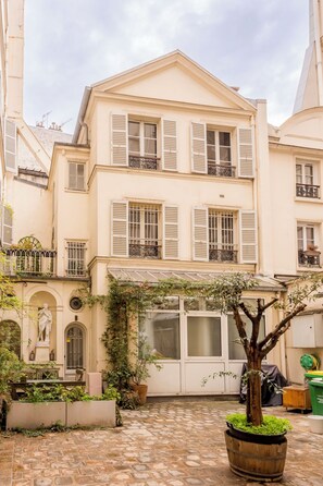 Un immeuble à plusieurs étages doté d’une cour intérieure où se trouvent un arbre, une statue et une fontaine.