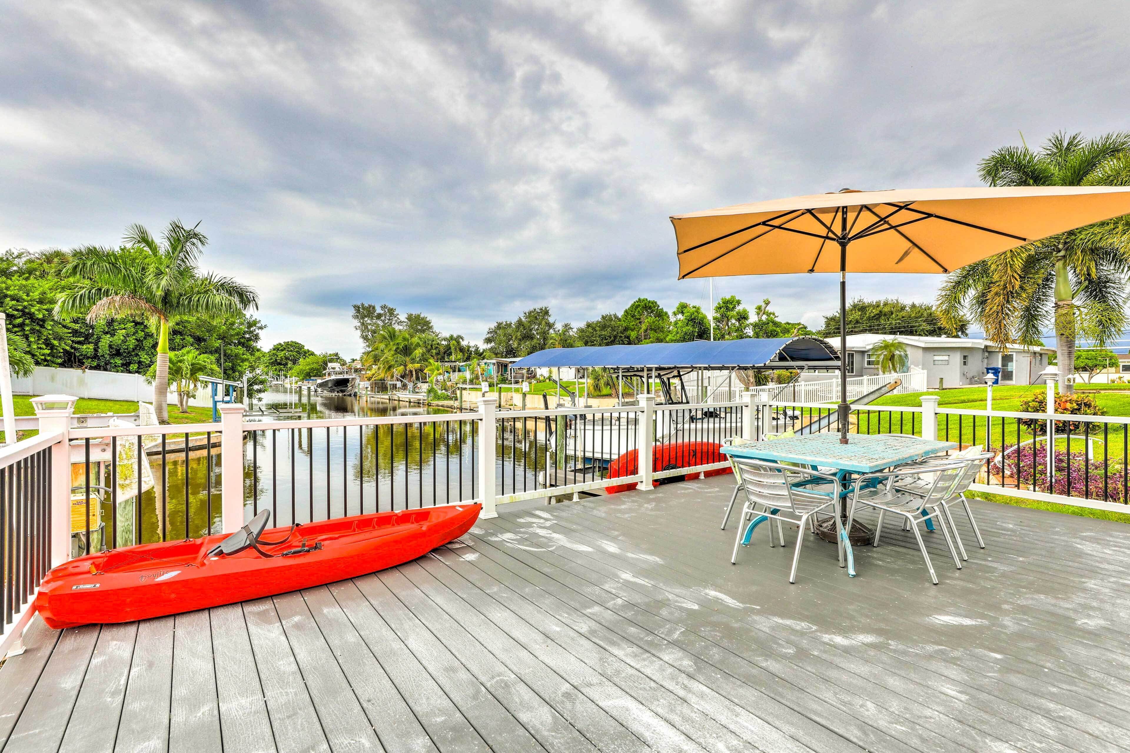 A wooden deck with a red kayak, a table with chairs, and a large umbrella.