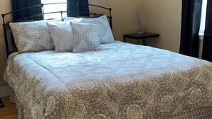A neatly made bed with a patterned bedspread, a bedside table with a lamp, and a window with curtains.