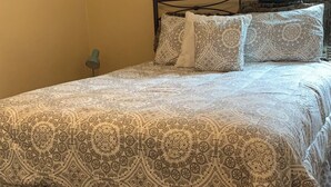 A bedroom with a patterned bedspread, a metal bed frame, and two wall art pieces.