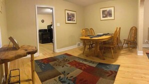 A dining area with a wooden table and chairs, a colorful rug, and two framed pictures on the walls.