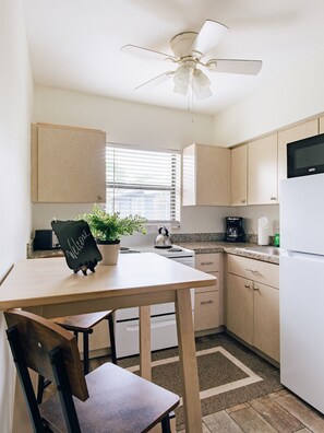 A modern kitchen with a ceiling fan, a kettle, a coffee maker, and a welcome sign on the table.