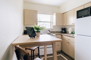 Uma cozinha compacta com mesa de madeira, chaleira, cafeteira e micro-ondas.