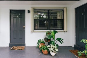 Uma porta de entrada com a placa '4', uma janela acima e vários vasos de plantas em frente.