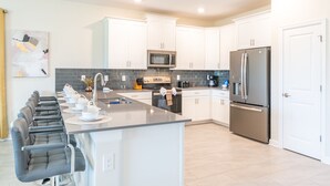 Una cocina moderna con gabinetes blancos, un refrigerador de acero inoxidable, un microondas y una isla grande con asientos.