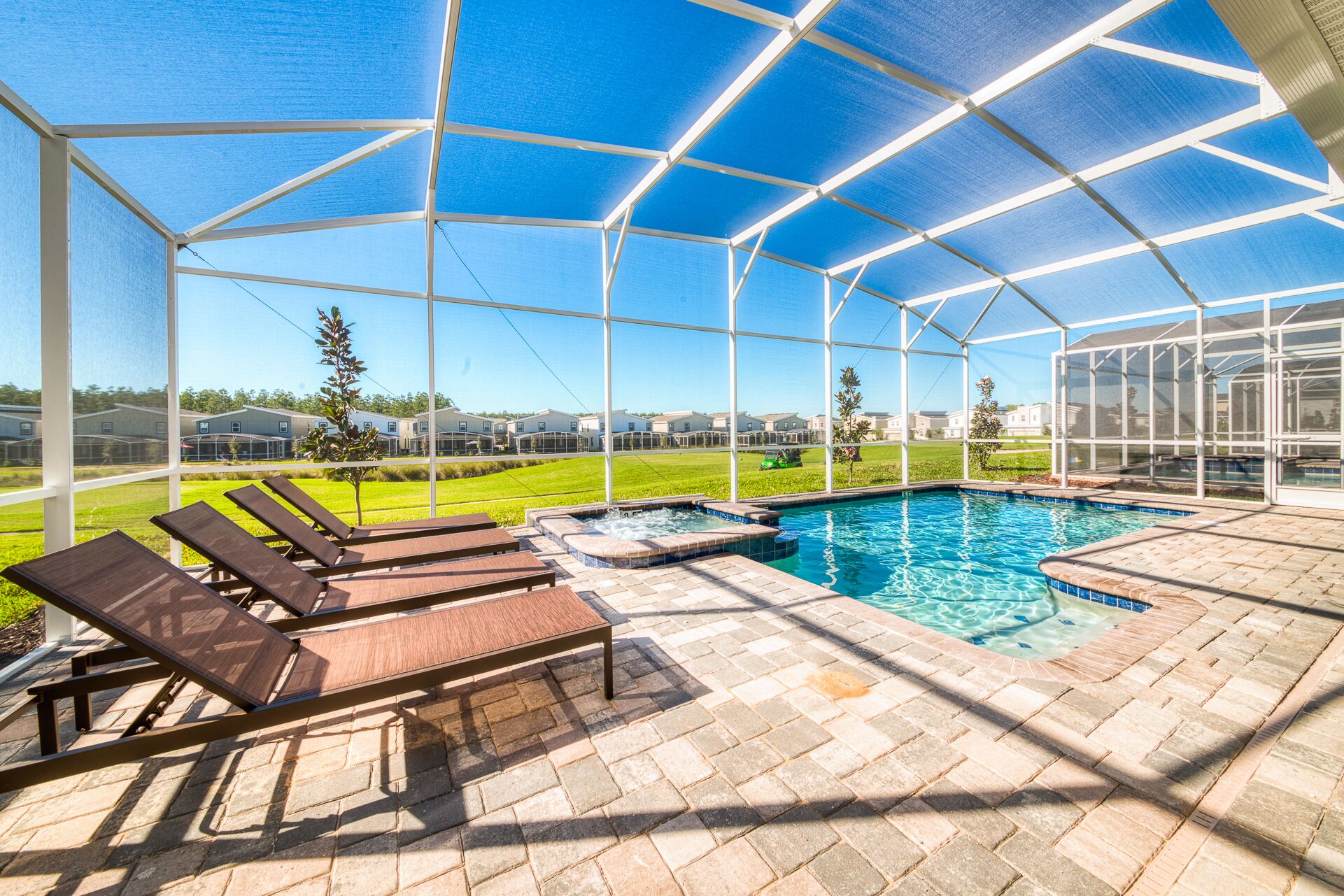 A covered outdoor swimming pool with lounge chairs, a hot tub, and a view of a residential area.