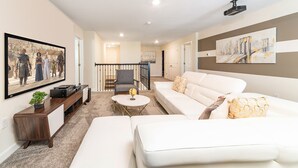 Una sala de estar moderna con un sofá blanco, una mesa de centro y un televisor montado en la pared. Se ve una escalera que sube a otro nivel.