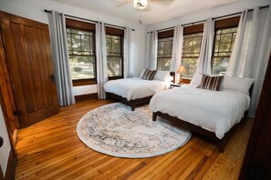 Un dormitorio con dos camas, suelo de madera y ventanas grandes con cortinas.