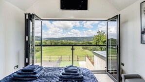 A bedroom with a large bed, a TV, and a balcony with a view of the countryside. - 3 bedroom accommodation in Pontyates (Pontyates)