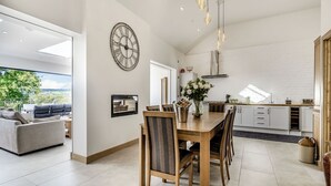 A modern kitchen with white brick walls, a dining area with a wooden table and chairs, and a large clock on the wall. - 3 bedroom accommodation in Pontyates (Pontyates)