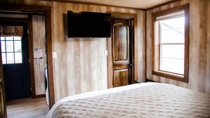 Un dormitorio con una cama, un televisor montado en la pared y una ventana.