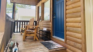Una cabaña de madera con puerta azul, un porche con una silla y una pequeña mesa.