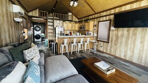 Una sala de estar moderna con un sofá, sillas, una mesita de centro y una cocina con microondas y lavaplatos.