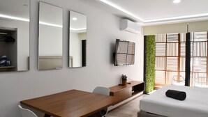 A modern hotel room with a wooden desk, a bed, a TV, and a green wall. - Luxury Apartment on 5th Av -One Paralia (Playa del Carmen)