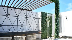 An outdoor bar area with a geometric wall design, wicker chairs, and a glass door labeled "MENESS". - Luxury Apartment on 5th Av -One Paralia (Playa del Carmen)
