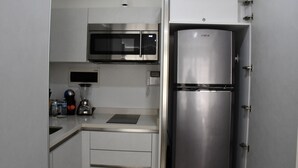 A compact kitchen with a built-in microwave, a stainless steel refrigerator, and a coffee maker on the counter. - Luxury Apartment on 5th Av -One Paralia (Playa del Carmen)