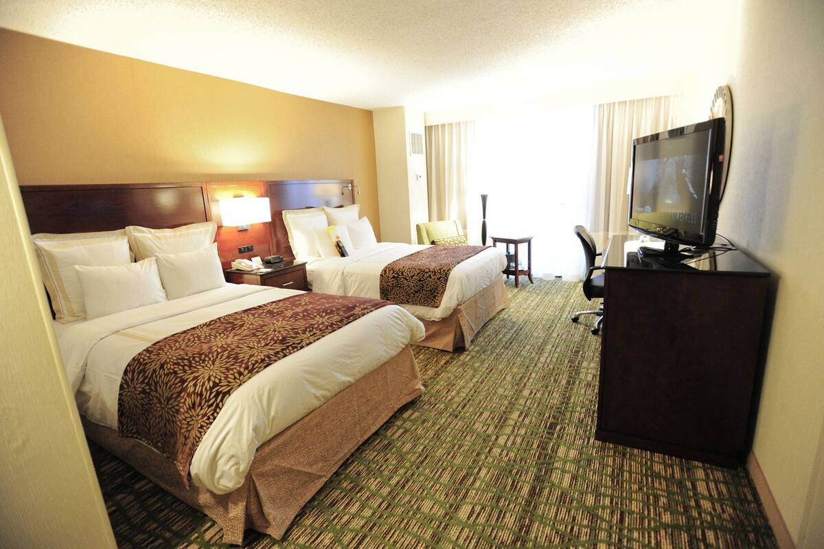 Une chambre d’hôtel avec deux lits, un bureau avec une télévision et une chaise.