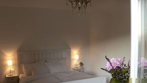 Ein Schlafzimmer mit Bett, Nachttischen, einem Sessel, einer Chandelier und einer Vase mit Blumen.