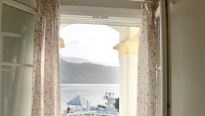 Ein Zimmer mit Balkon, Blick auf ein Gewässer und eine Berglandschaft.