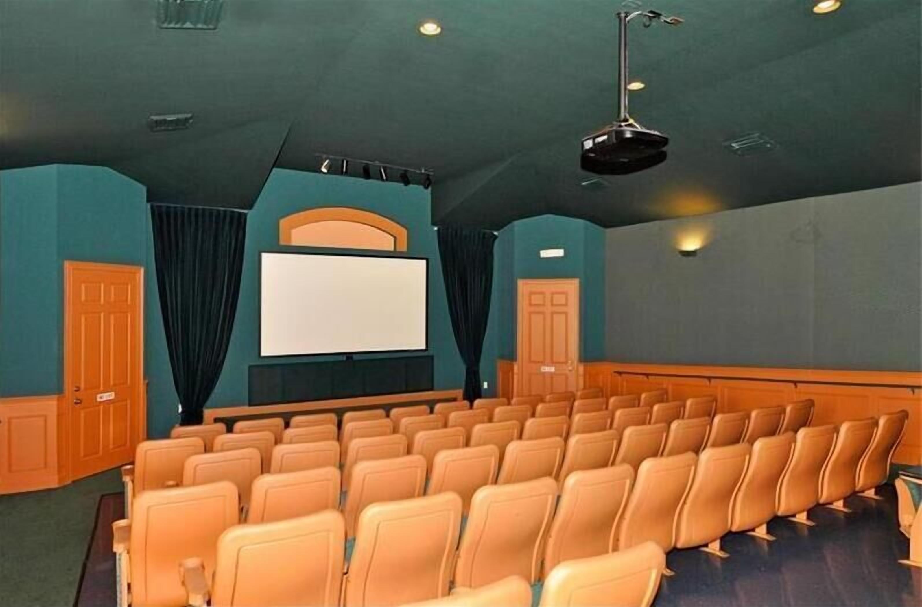 Ein Theater mit Sitzreihen, einer großen Leinwand und einer Bühne.