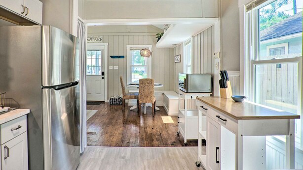 Eine moderne Küche mit einem Edelstahlkühlschrank, Holzboden und einer Essecke mit Korbstühlen.