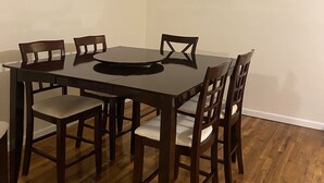 Een eetruimte met een rechthoekige tafel en zes stoelen, een plafondlamp en houten vloeren.