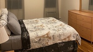 Een slaapkamer met een bed, een ladekast, een spiegel en dunne gordijnen.
