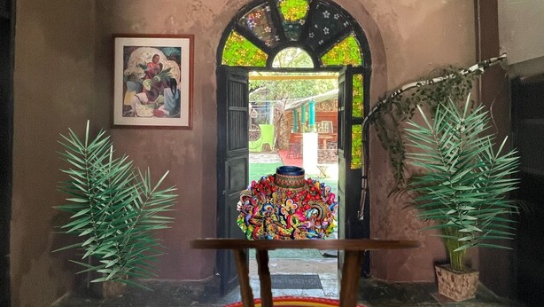 Una habitación con techo de madera, un tapete circular de colores, un cuadro enmarco y una planta en maceta.
