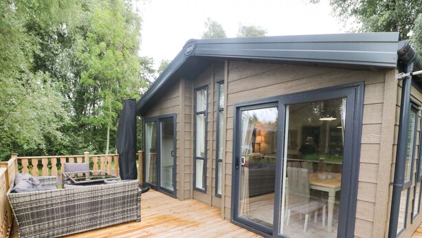 A modern house with a wooden deck, a wicker sofa, and a dining area with glass doors.