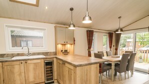 A kitchen with wooden cabinets, a built-in dishwasher, a large island, pendant lights, and a dining area with chairs and a table.