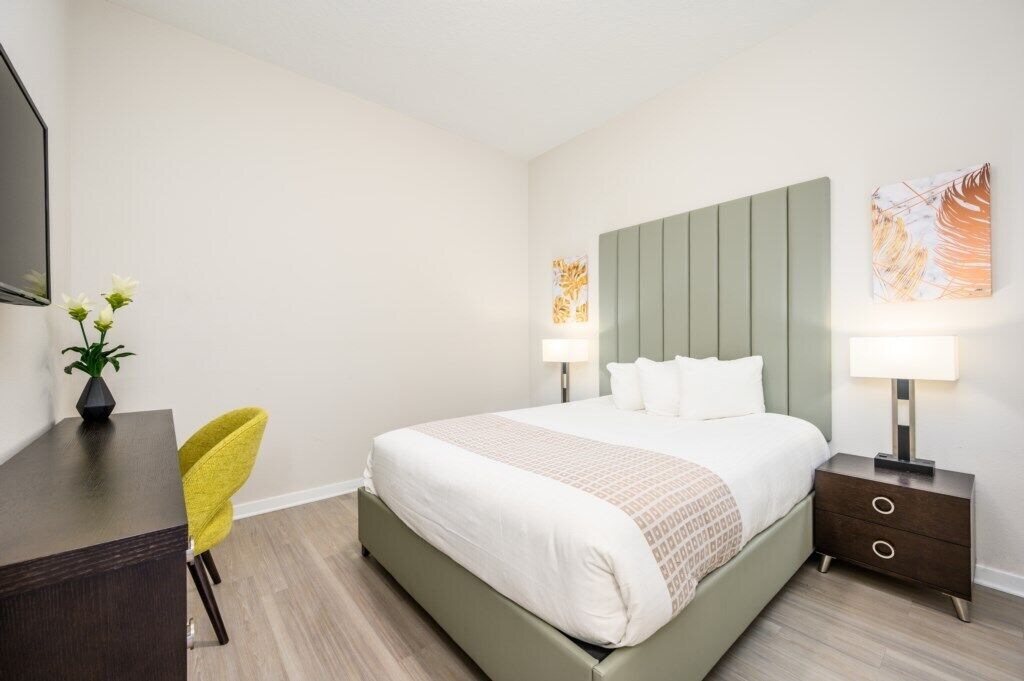 Ein Hotelzimmer mit Bett, Nachttischen, Schreibtisch, Stuhl und Bildern an den Wänden.