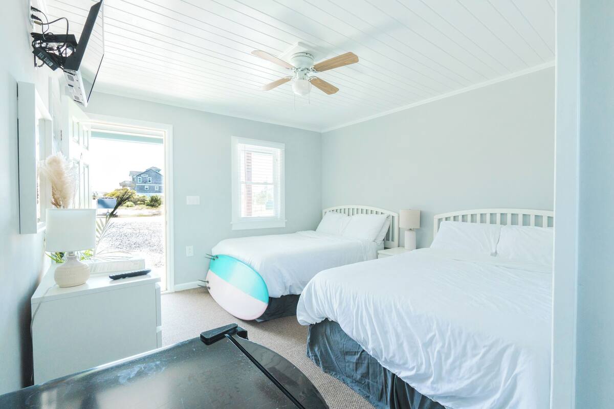 A bedroom with two beds, a ceiling fan, a desk with a lamp, and a window.