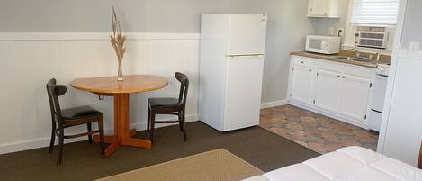Habitación de hotel compacta con cama, una pequeña mesa de comedor con dos sillas, refrigerador, microondas y kitchenette.