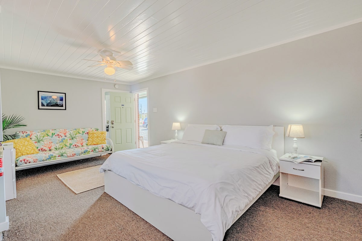 A bedroom with a bed, nightstands, a sofa, and a door.