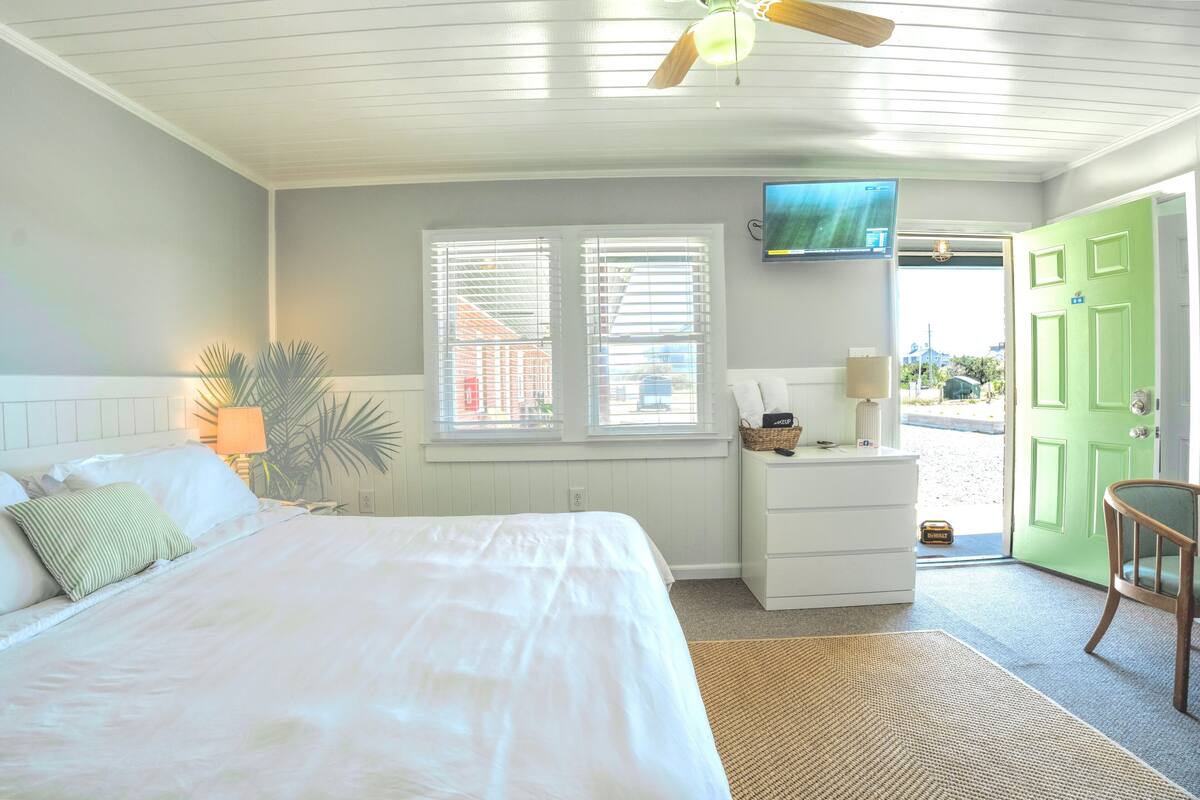 A bedroom with a bed, a nightstand, a lamp, a television, and a green door.