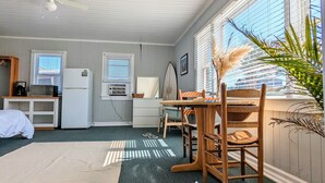 Une pièce comprenant une table à manger et des chaises, un ventilateur de plafond et une grande fenêtre avec des stores.