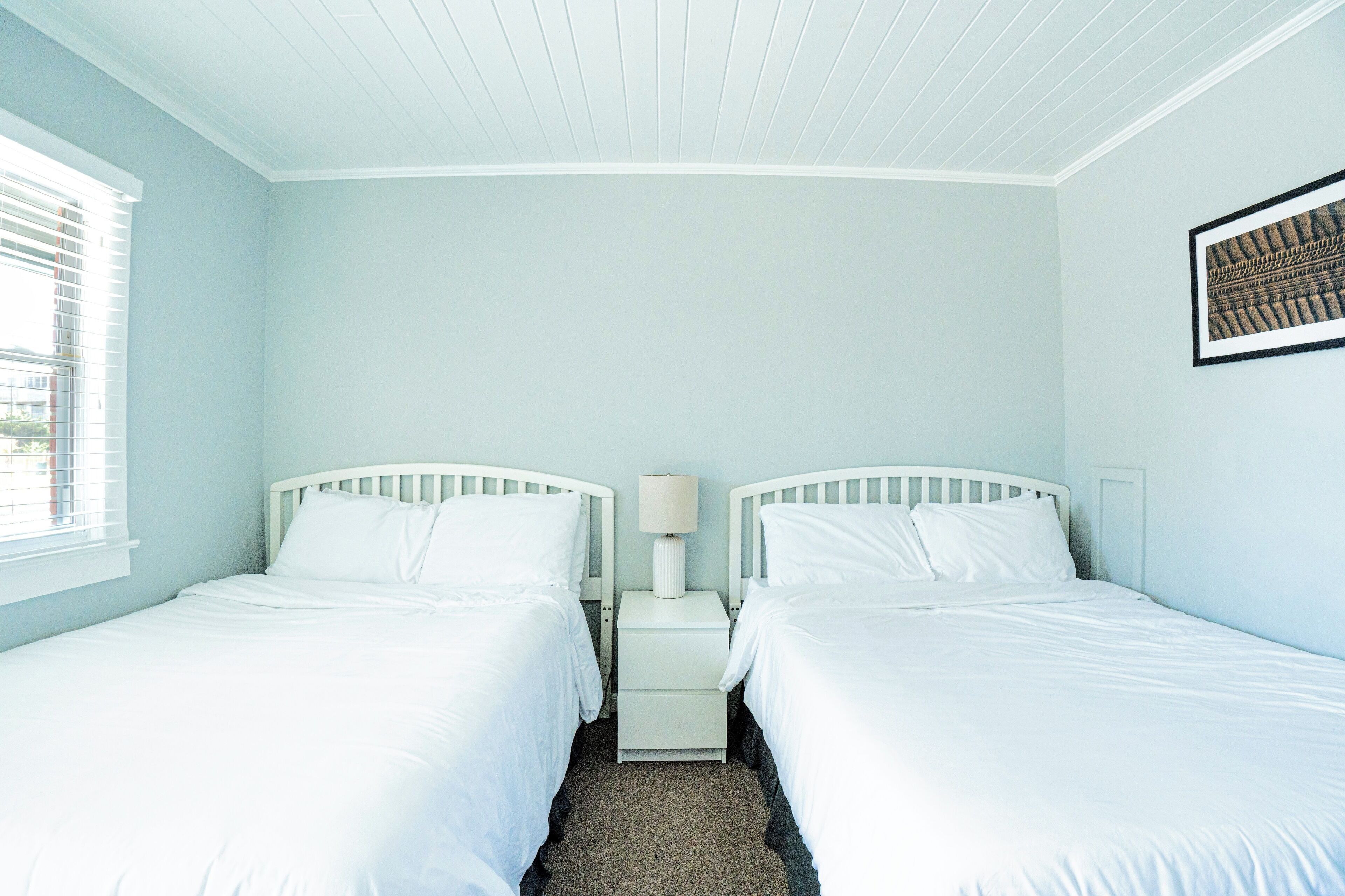 A bedroom with two single beds, a nightstand with a lamp, and a framed picture on the wall.