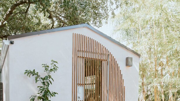 Un edificio pequeño y blanco de una planta con una terraza de madera y una mesa con sillas.