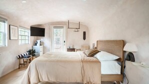 Un dormitorio con cama, mesita de noche, lámpara y televisor instalado en la pared.