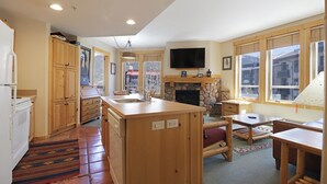 A kitchen with wooden cabinets, a stone fireplace, a television mounted above it, and large windows. - Condo w/ Outstanding Location, Outdoor Hot Tub, Short Walk to Lifts - TX314 (Copper Mountain)
