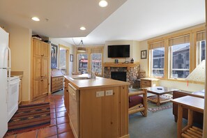 A kitchen with wooden cabinets, a stone fireplace, a television mounted above it, and large windows. - Condo w/ Outstanding Location, Outdoor Hot Tub, Short Walk to Lifts - TX314 (Copper Mountain)
