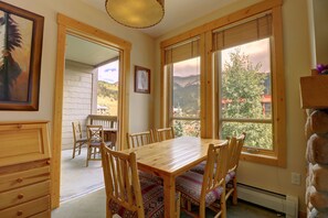 Enjoy meals in this dining area with a table and chairs, surrounded by large windows offering views of the mountains and a tree.