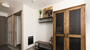 Un pasillo con puerta de madera, un banco, un estante con plantas y una chimenea.