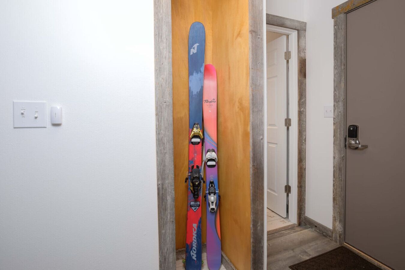 Un couloir avec un cadre de porte en bois et deux paires de skis appuyés contre le mur.