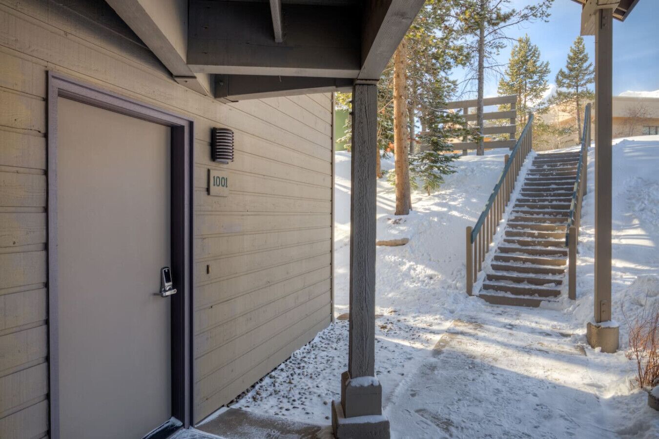 L’entrée d’un immeuble se compose d’une porte portant le numéro « 1001 », d’un porche abrité et d’un escalier menant à une terrasse en bois.