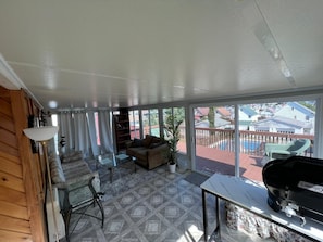 Una habitación iluminada por el sol con un amplio ventanal corredera que da a una terraza con piscina, una parrilla y un sofá.